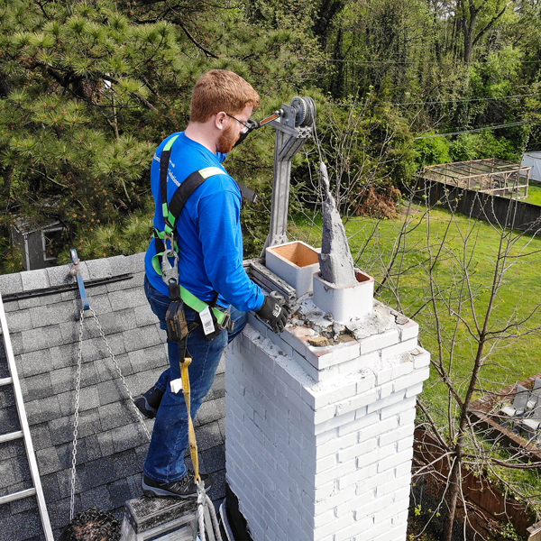 A chimney professional prepares to apply sealant in a chimney repair process on a rooftop.
