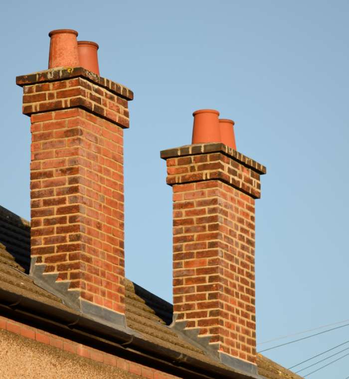 Two brick chimneys with terracotta pots against the clear sky on a roof.